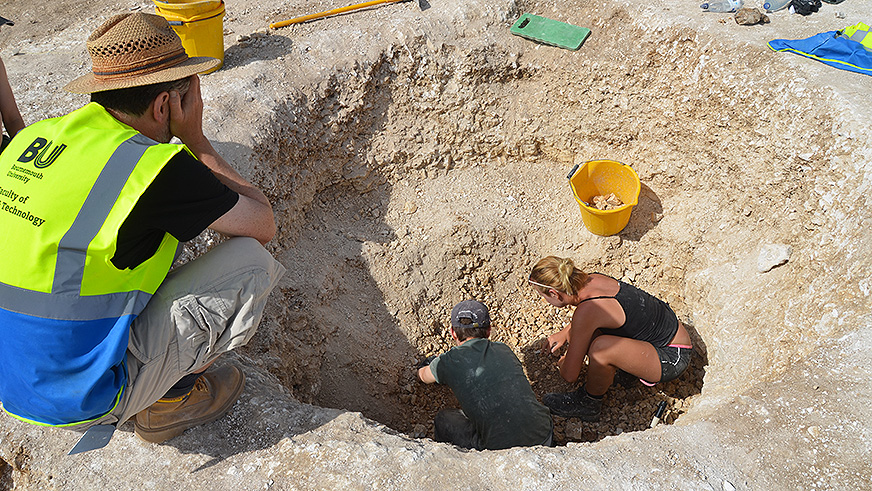Two students digging for archaeological finds, overseen by a BU archaeologist
