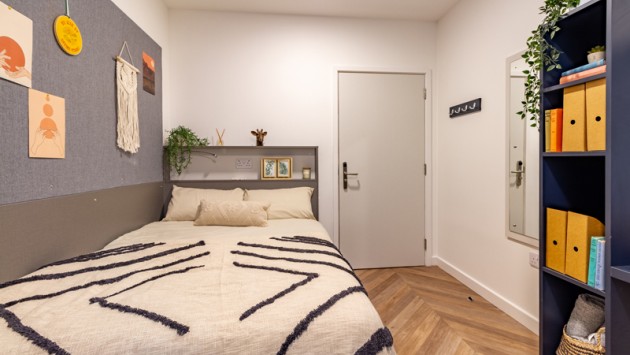 A room in Belaton House, featuring a view of the bed, bookshelf, entrance and a pinboard alongside the bed