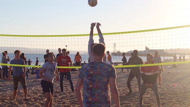 An image of people playing volleyball at a beach BBQ