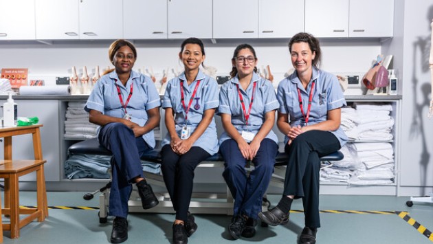 Four female students in skills uniform sitting together in the nursing simulation suite