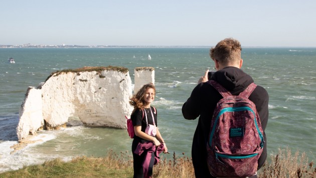 Image of a student having a her photograph taken by another student on a clifftop overlooking the sea.