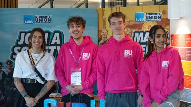 Three Bournemouth University student ambassadors wearing bright pink hoodies stood in front of Students' Union Bournemouth University (SUBU) banners in the Student Centre