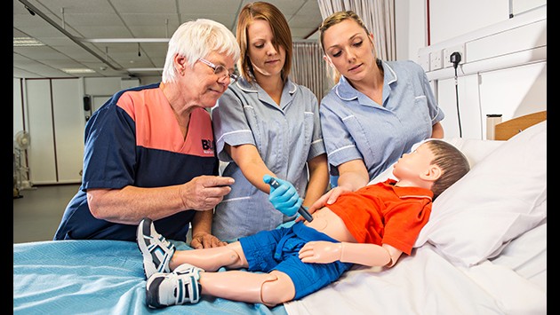 Student nurses with a tutor examining a child mannequin on the ward