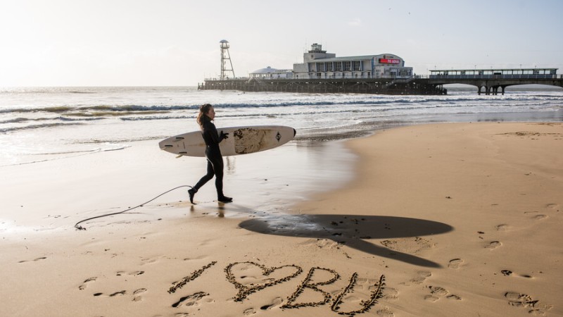 Surfer on Bournemouth beach with I love BU written in the sand
