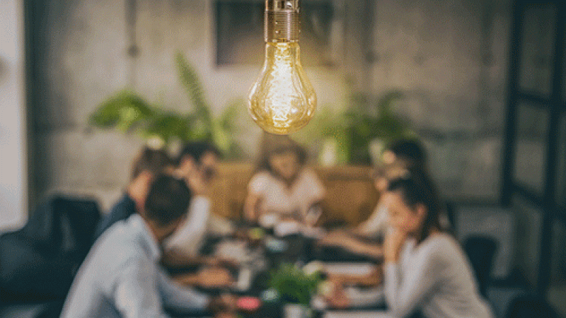 people sitting around a table with a lightbulb overhead