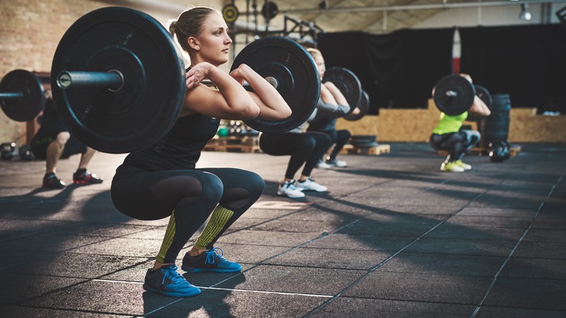 A weightlifting class with women and men squatting with large barbell weights before a lift
