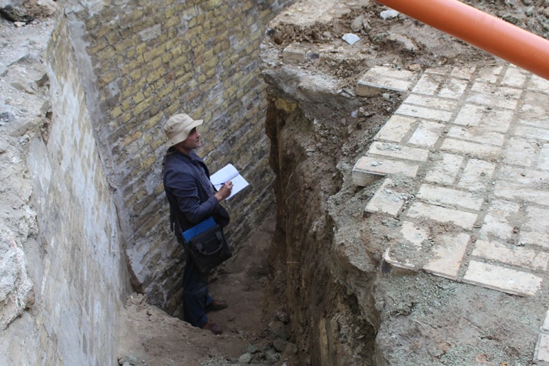A man standing in a deep Archaeological pit, surrounded by rectangular straight walls