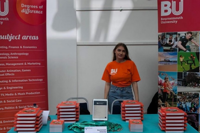 A BU display at an event, with a student ambassador surrounded by prospectuses and pull-up banners