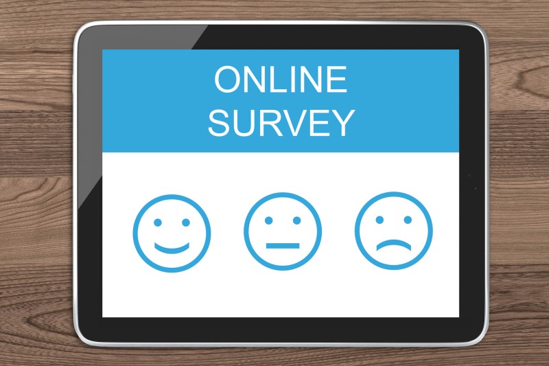 An ipad on a wooden surface with an online survey and different smiley face options 