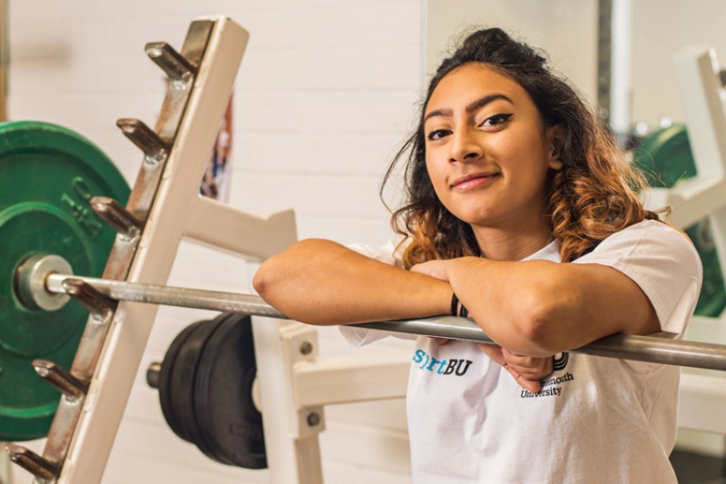 Noorin Gulam, a BU sport scholar, with weightlifting equipment in the BU gym