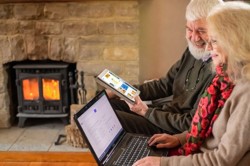 An older couple sat on a sofa on a laptop and tablet