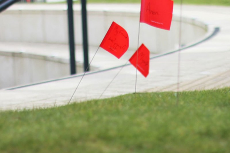 Red notes with names on pinned into the soil on Talbot Campus