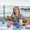 Student sat at a bench smiling at camera with beack in background