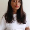 Student Madhumitha poses in a headshot style image wearing a white t-shirt. her hair cascades just below her shoulders, she has a soft red lipstick on and half pouts/ half smiles at the camera