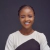 Student Olamaide smiles brightly in front of a grey backdrop, photographed in a headshot style, wearing a black and white top.