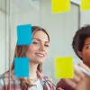 Three people looking at a  clear screen with stuck post-it notes
