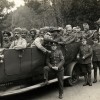 Old black and white photo from the First World War. Members of Indian army in a large open topped vehicle with 3 soldies standing in front of it. 