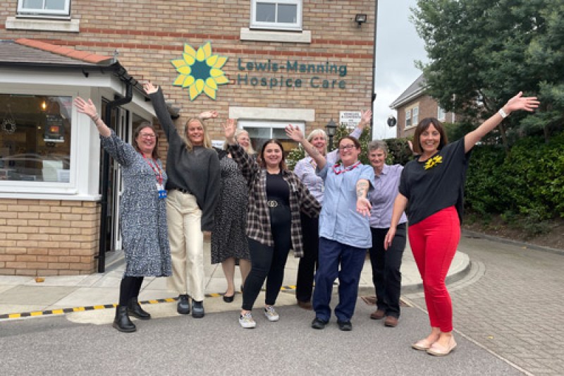 Eight women standing in a line, waving at the camera outside the Lewis-Manning Hospice building