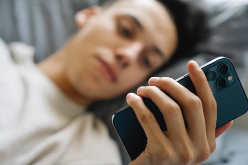 A man lying down looking at his mobile phone screen