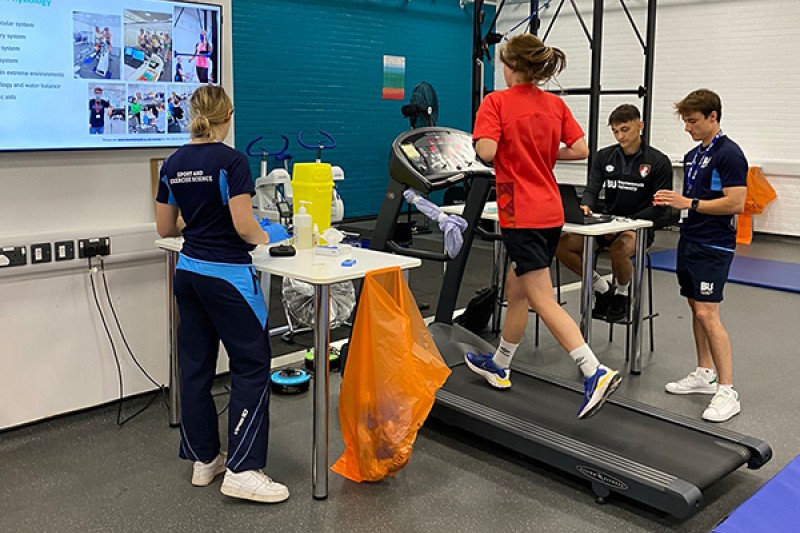 AFCB Fitness Testing treadmill 3 Side view of AFCB player running on the treadmill whilst three sport scientists look and screens connected to the machine