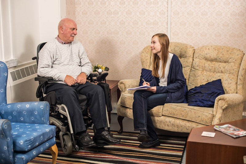 A young woman talking in a care home to an elderly man who uses a wheelchair