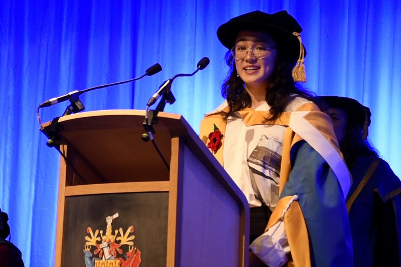 Alice Tai in her ceremonial robes, standing at a lectern talking