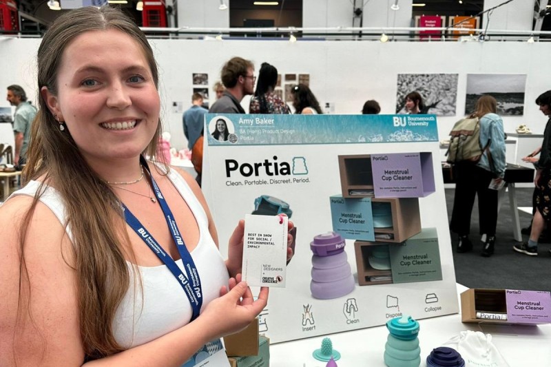 Amy holding her award in front of a poster for her product (Portia)