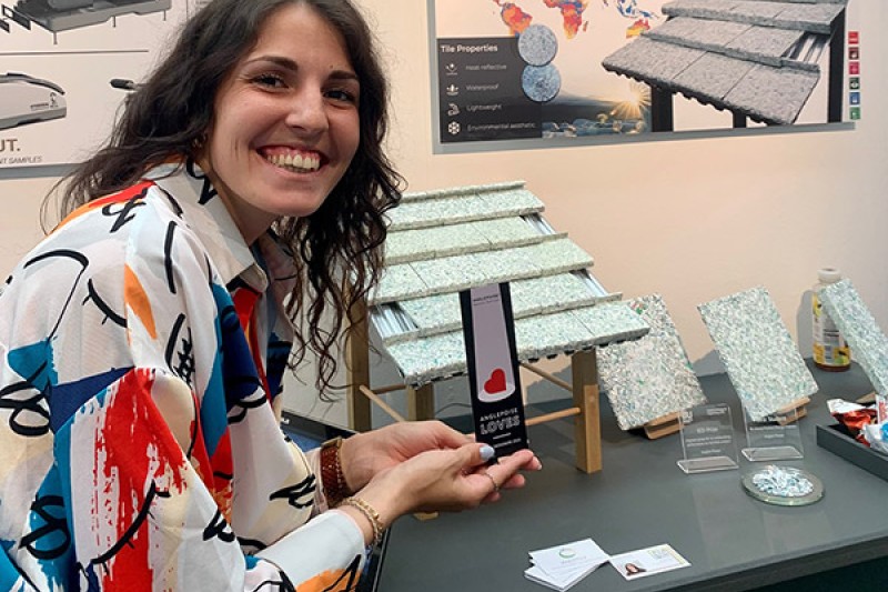 Angela and her award with prototype roof tile Angela holds her award next to a prototype of her reusable roof tiles