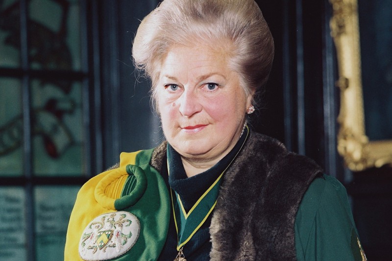 A lady in a ceremonial cloak and necklace looking at the camera