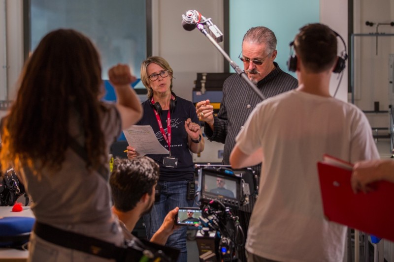 Annie and Griff Griff Rhys-Jones stands in from of a camera. To his left is the director assistant. In front is the film camera with griff's image on the small display. A boom operator stands at the front with his back to the camera holding up the boom mic
