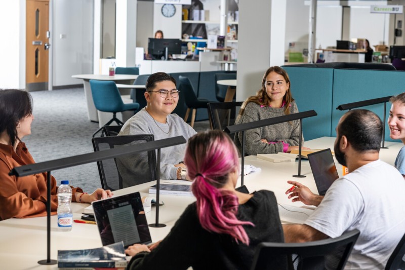 A group of students sitting around a table talking in a library