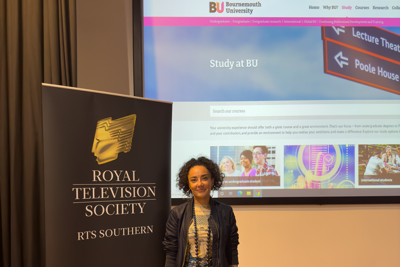 Yasmin Yasmin standing next to a Royal Television Society banner with the BU website projected onto the screen behind her