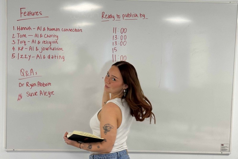 Isabel stands in front of a white board with stories and publishing schedule written on