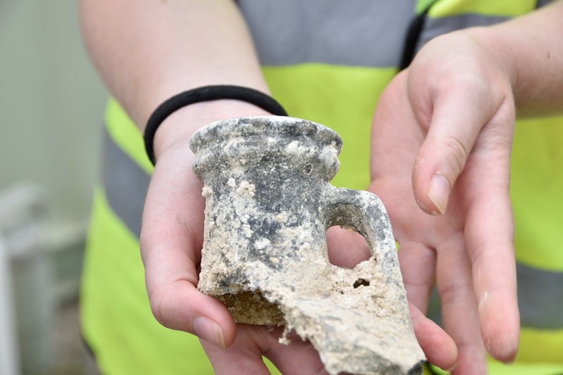 A student holding a fragment of a Roman style wine flagon, showing the handle and the pouring spot