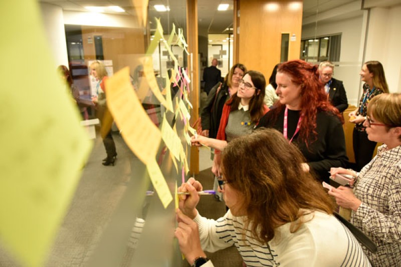 BU and UHD staff post their ideas on a shared wall BU and UHD staff putting post it notes up on a wall