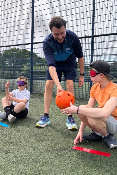 Dr Ben Powis handing a goalball ball to one of the visiting children