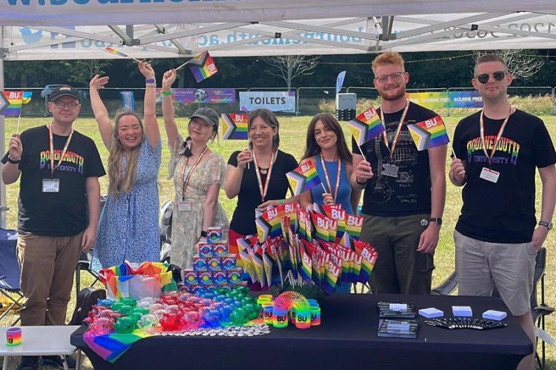 Four women and three men holding Pride flags, standing in front of a table full of toys in the rainbow flag colours