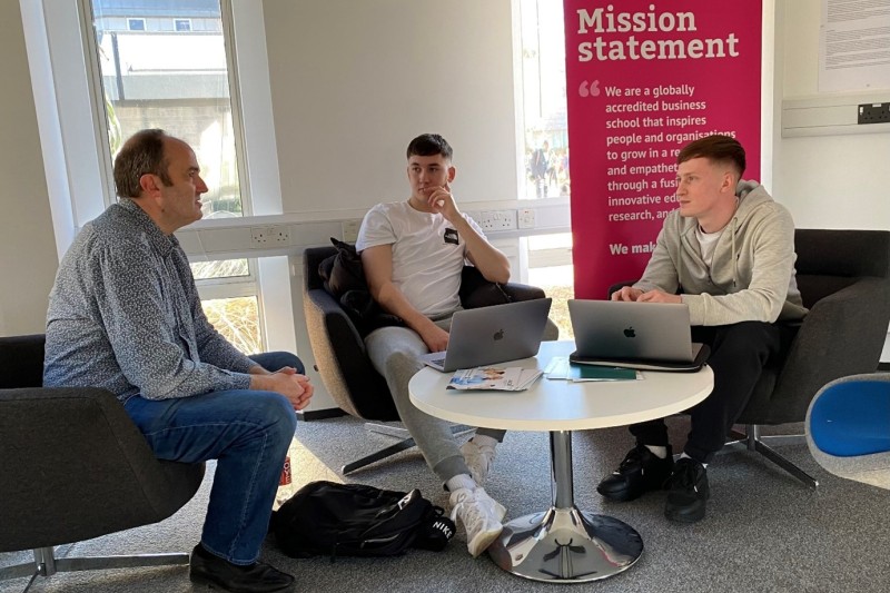 Business School Clinic Two male students sitting round a table talking to their lecturer