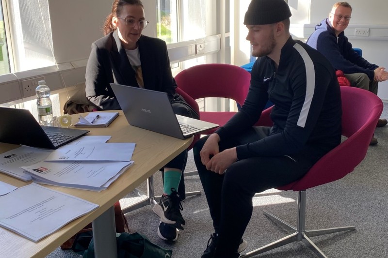 A male student sitting at a table talking to his lecturer 