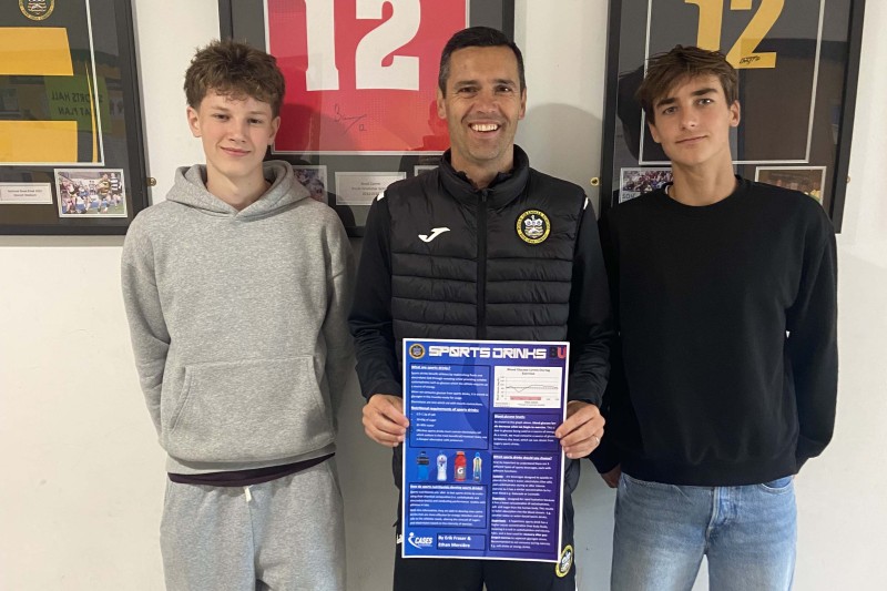 Two pupils standing either side of their teacher. The teacher is holding their prize winning poster. 
