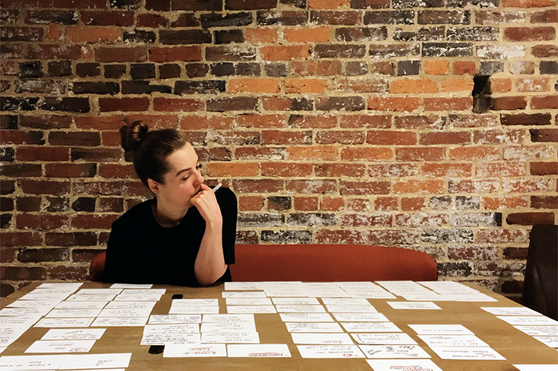 Claudy sits at a table studying a note cards that are laid out all across the table in front of her 