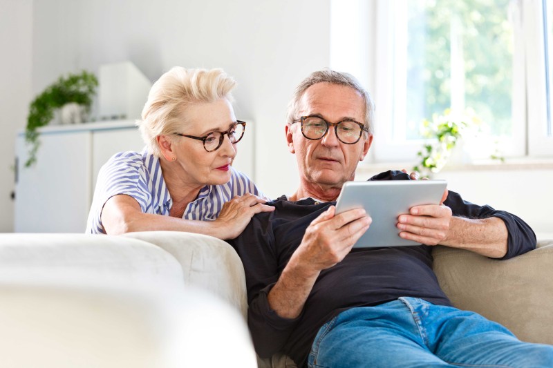 An older man and woman on a sofa looking at a tablet device An older man and woman on a sofa looking at a tablet device