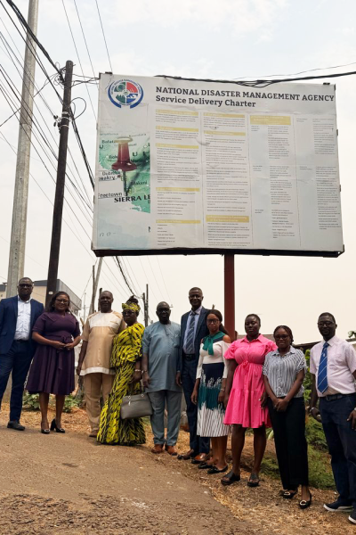 NDMA staff members standing below one of Freetown's billboards NDMA staff members standing below one of Freetown's billboards