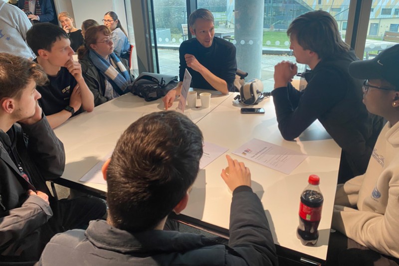 A group of students sitting around a table talking to Andy Davies