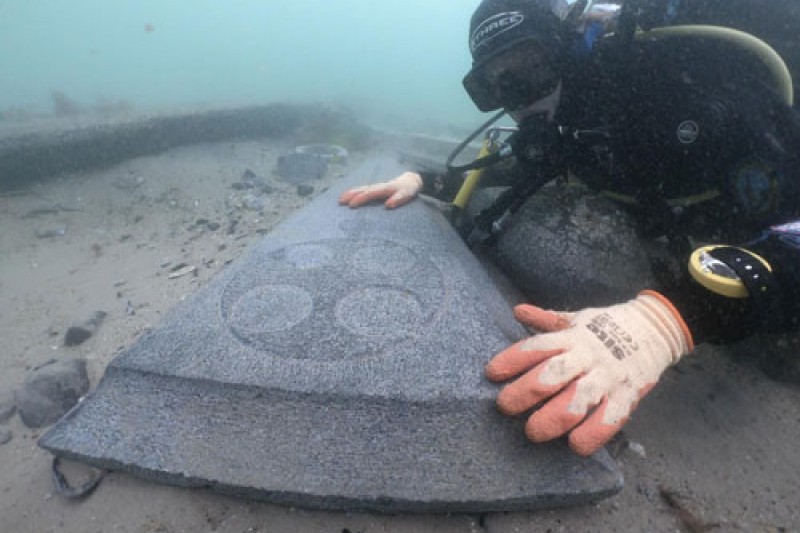 Bournmeouth University maritime archaeologist diving next to one of the decorative gravestones on the seabed