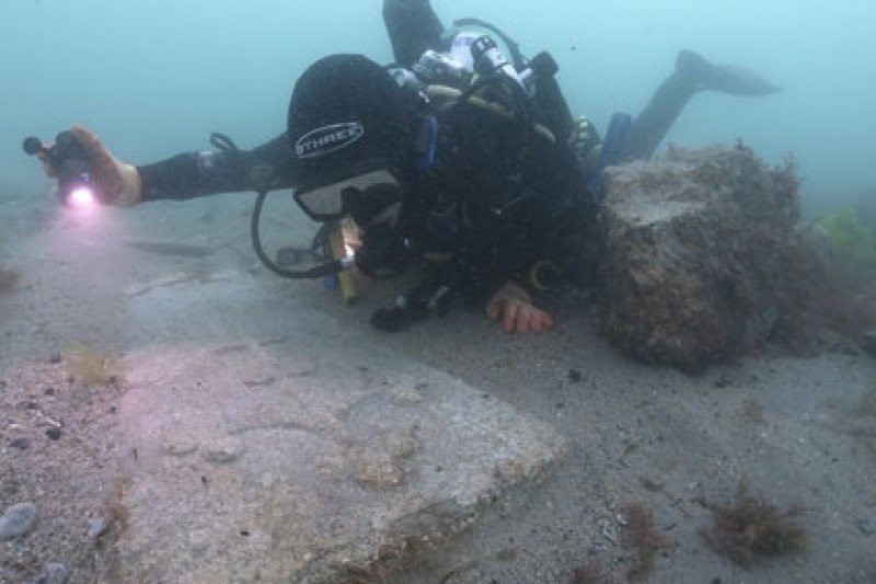 Bournmeouth University maritime archaeologist diving next to one of the two decorative gravestones on the seabed