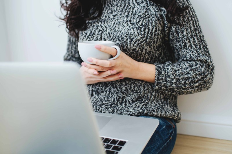 Young woman looking in the screen of laptop. Holding the white mug.
