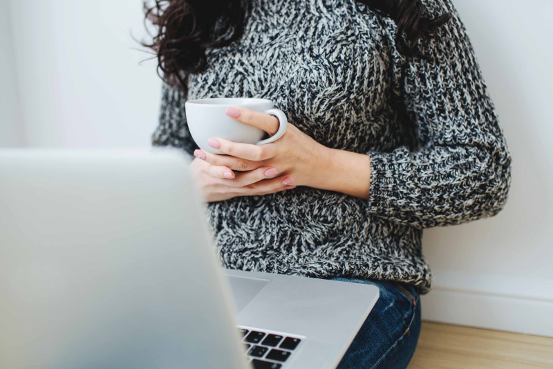 Young woman looking in the screen of laptop. Holding the white mug. 