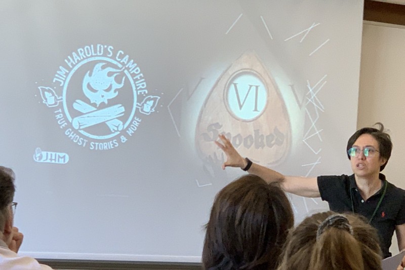 A woman standing in front of a group of people pointing to a screen with her presentation on