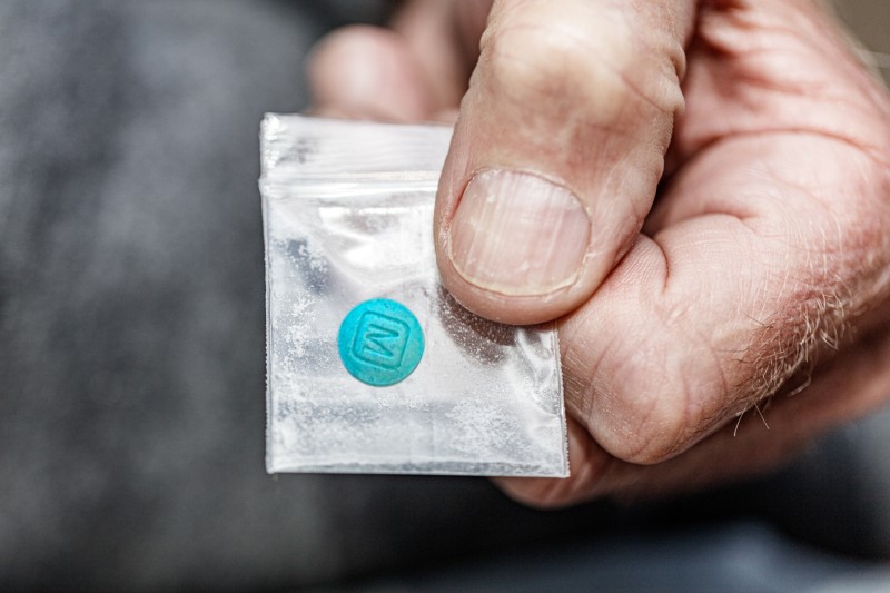 Hand holding a small plastic packet with a fentanyl tablet inside Hand holding a small plastic packet with a fentanyl tablet inside